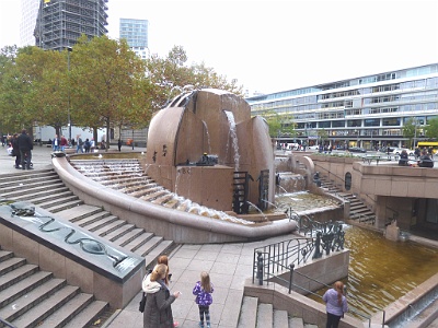 World Globe Fountain - "Wasserklops"  The main part of the complex consists of several carved blocks of red granite , which together form an approximately hemispherical base with a total diameter of 8.5 meters and are arranged in a water basin of 16 meters in diameter. On them are numerous fountains , water fountains and other water features. In the symbolic globe characters of different cultures are embedded. [6] The large water basin is surrounded by a staircase that leads from Breitscheidplatz into the basement of the Europa Center. In the southeastern flight of stairs is inserted as another water feature of the watercourse of bronze with the five scenes of mountains, pastures, urban landscape, landfill and mermaids . To the north of the main basin, set off about 15 m, is the also belonging to the plant Small fountain with the bronze figure game with puppet . [8th]