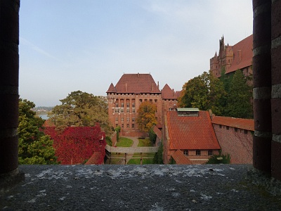 Malbork Castle  The elaborately decorated wall-walk immediately above these major apartments is carried on four-centred arches spanning the machicolated recesses between the brick buttresses and protected by the eaves of the steeply pitched roof. The walk  expands into six-sided turrets at the corners, brace-supported in stone, while the same material is used for the blind trefoil and quatrefoil paneled  battlements to create a highly decorative head to the Palace wing