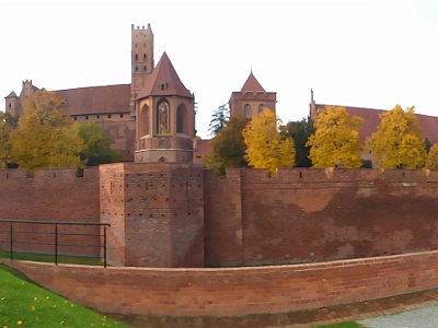 Malbork Castle Panorama  Malbork Castle - 14th-century Teutonic castle housing museum of medieval artifacts, paintings & an amber collection. The largest castle in the world measured by land area. It consists of three separate castles - the High, Middle and Lower Castles, separated by multiple dry moats and towers. The castle once housed approximately 3,000 "brothers in arms". The outermost castle walls enclose 21 ha (52 acres), four times the enclosed area of Windsor Castle. Malbork Castle remains the largest brick building in Europe.